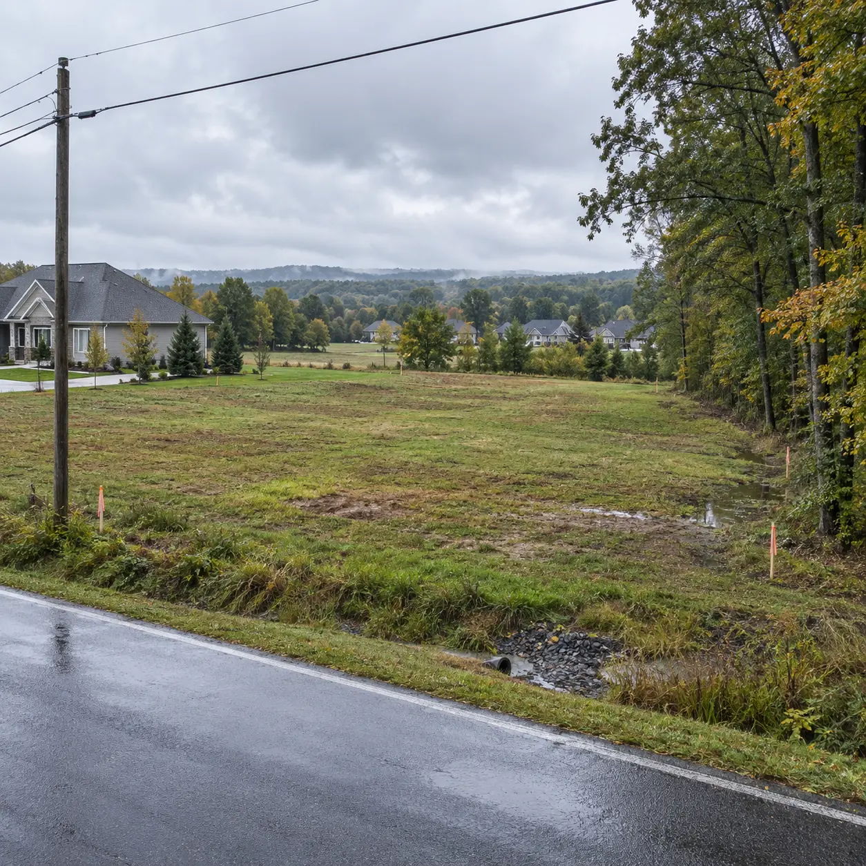 Vacant suburban land with road access, utility lines, drainage, survey markers, nearby development, and terrain features used by AI land valuation algorithms to estimate property value.
